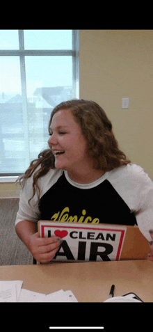 a girl sitting at a table holding a sign that says i love clean air