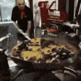 a large pizza is being cooked in a frying pan in front of a sign that says bake