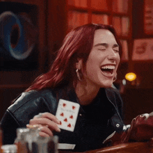 a woman with red hair is laughing while holding a card in her hand .