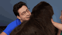 a man wearing glasses and a blue shirt is hugging a large stuffed animal