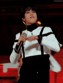 a man is singing into a microphone while wearing a white jacket and black pants .