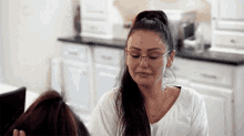 a woman wearing glasses and a white shirt looks down