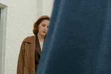 a woman in a brown coat stands in a room
