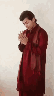 a man in a red robe is praying with his hands folded .