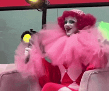 a woman in a pink clown costume is sitting in a chair with a microphone .