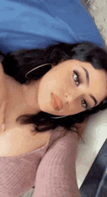 a woman in a pink sweater is laying on a bed and taking a selfie .