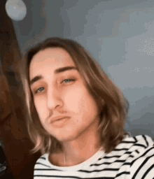 a man with long hair and a mustache is wearing a striped shirt .