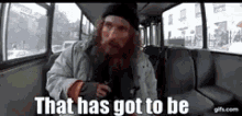 a man with a beard is sitting on a bus with the words `` that has got to be '' written on the screen .