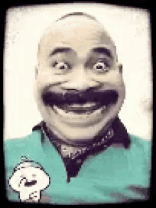 a bald man with a mustache is smiling and wearing a green shirt .