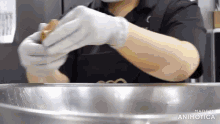a person wearing white gloves and an apron is preparing food in a metal bowl