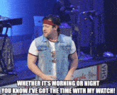 a man in a denim vest stands on a stage with a sign that says vhs on it