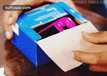a person is opening a blue box with the words kulfyapp.com in the corner