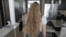 a woman with long blonde hair is standing in a kitchen next to a refrigerator .