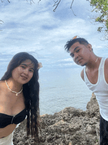 a man and a woman are posing for a picture on a rocky beach near the ocean