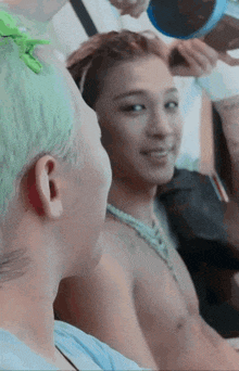 a shirtless man with green hair looks at another man