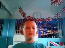 a young boy in a bedroom with british flags hanging from the ceiling and a clock on the wall