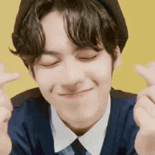a young man wearing a hat and tie is smiling and making a heart shape with his hands .