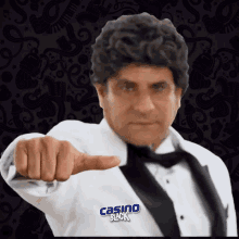 a man wearing a tuxedo and tie is pointing at the camera with a casino black logo behind him