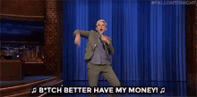 a man in a suit is singing into a microphone while dancing on a stage and saying " better have my money "