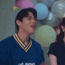 a man wearing a party hat is standing in front of balloons and laughing .