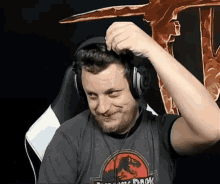 a man wearing headphones and a jurassic park shirt is making a funny face .