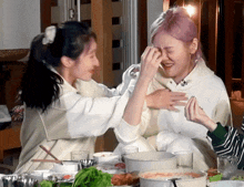a woman wipes another woman 's face while sitting at a table