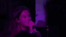a young girl is singing into a microphone in front of a purple background .