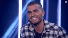 a man in a plaid shirt is smiling while sitting in front of a blue background .