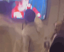 a man wearing a hat and scarf is watching a sports game on a television