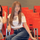 a woman wearing a miss 35 shirt sits in a row of red chairs