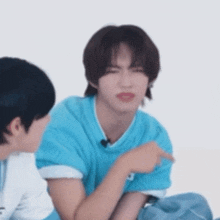 a young man in a blue shirt is sitting next to another young man and making a funny face .