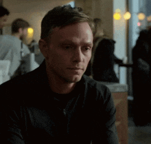 a man wearing a black jacket is sitting at a table in a restaurant