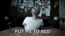 a woman is sitting on a bed in a dark room and saying `` put me to bed '' .