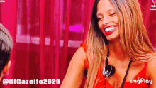 a woman in a red dress is smiling in front of a pink curtain that says bigazeite2020