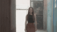 a woman in a black top and brown skirt is walking down an alley .