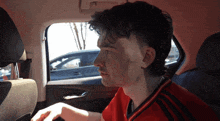 a young man in a red shirt is sitting in a car