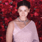 a woman wearing a necklace and earrings is standing in front of a wall of red flowers
