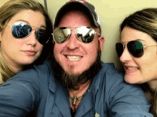 a man with a beard and two women wearing sunglasses pose for a picture
