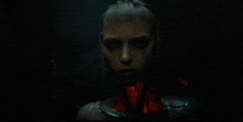 a close up of a woman 's face in a dark room with red lights coming out of her neck .