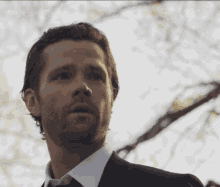 a man with a beard is wearing a black suit and tie