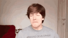 a man wearing a gray shirt that says `` arrested development '' is making a funny face with his eyes closed .