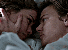 a man and a woman are laying in bed looking at each other and touching their faces .