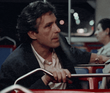 a man in a suit sits on a bus with his hand on a railing