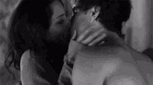 a black and white photo of a man and woman kissing in bed .