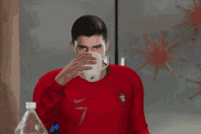 a man in a red nike shirt drinks from a glass next to a bottle of aquafina water