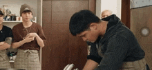 a man in a black hoodie is cooking in a kitchen with other people