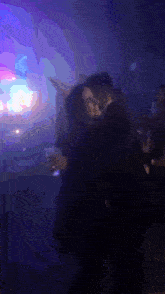 a man and a woman are dancing in a dark room with purple lights behind them .