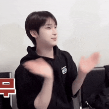 a young man wearing a black hoodie is clapping his hands while sitting in a chair .