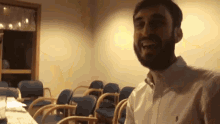 a man with a beard is standing in a room with chairs and smiling