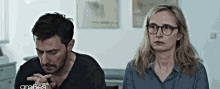 a man and a woman are sitting next to each other in a room . the man is wearing glasses .